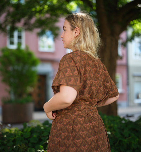 Vår klänning AVA Vildvin. Lyxigt enkel kaftanklänning till årets alla fester. Ava har rundad nacklinje bak, v-ringning, sidfickor och veck mitt fram. Obibälte ingår. Bältet är lätt vadderat och passar även fint att ha till annat:) Sydd i Ekoveroviskos från Frankrike.  Färg: Vildvin. Mönster i vinrött, olivgrön, skogsgrön och rosa.  Material: 51% EcoVero, 49% viskos från Frankrike.