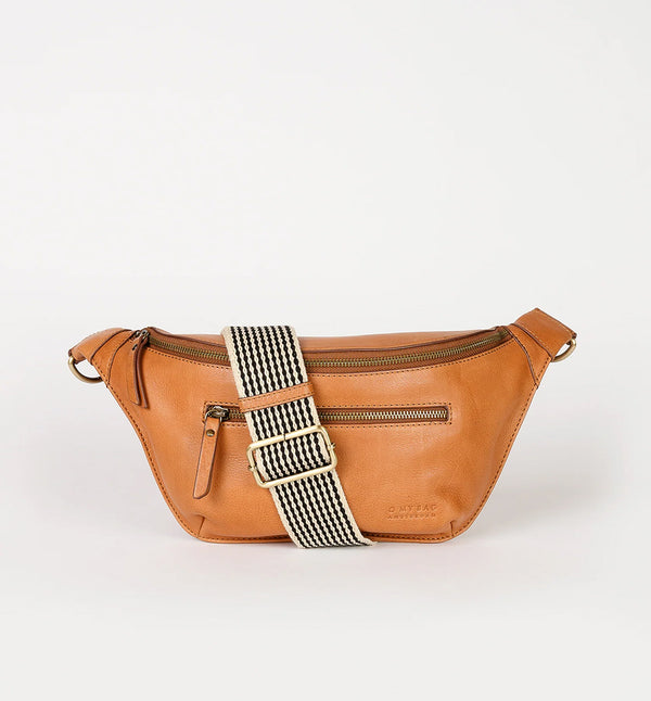Drew Bum Bag från O My Bag. Lika praktisk som snygg! Den här designen är gjord av O My Bags mjuka narvläder och är perfekt för dem som vill ha med sig mer än bara en telefon och plånbok. Drew passar en 0,5 liters vattenflaska samt andra nödvändigheter. Med en ficka med dragkedja på fram- och baksidan, invändiga glidfickor och en säker dragkedja; denna väska kommer också med två justerbara remmar. Ett läderband och ett rutigt band. Färg cognac