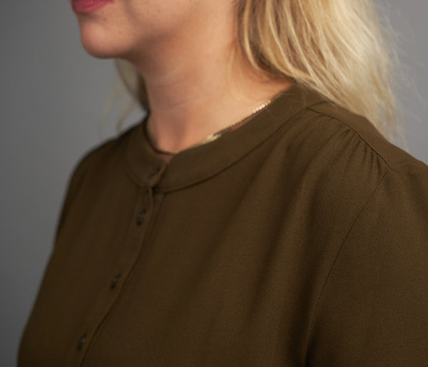 Lieblings klänning Miso Hassel. Rundad bandkrage, knappslå fram, ok med veck fram och bak. Ärm med rynk, smal manschett med knapp. Hällor och fickor i sidorna. Band i midjan. Sydd i ett deadstocktyg.