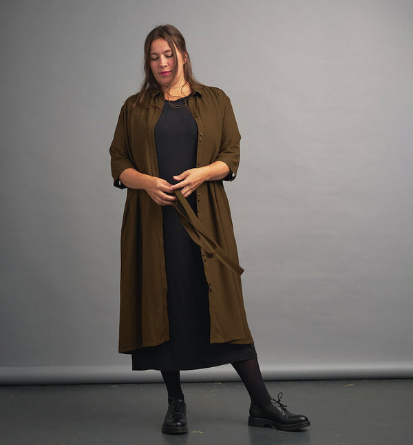 Lieblings klänning Svala Hassel. En ankellång skjortklänning med lös passform, trekvartsärm och fickor i sidorna. Ok med rynk i ryggen. Ett 2,5 cm brett band i samma tyg medföljer och kan knytas i midjan. Svala är fin både öppen och stängd, med eller utan band. Mörkgröna knappar mitt fram och vid ärmslut. Sydd i ett deadstocktyg.
Färg: Hassel, mörkt olivgrön.
Material: 100% viskos