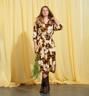 Liebling klänning Bonnie! Bonnie är en smula countryinspirerad i modellen. V-ringad, puffiga ärmar, fickor i sidorna och band att knyta i midjan. Rundat ok bak. Armbågslång ärm med smal manschett med en knapp. Svarta knappar mitt fram. Tyget är blankt vilket ger en lyxig känsla!&nbsp;

Färg: Vita blommor och svarta blad på guldbrun botten.&nbsp;

Material: 51% EcoVero, 49% viskos från Frankrike.