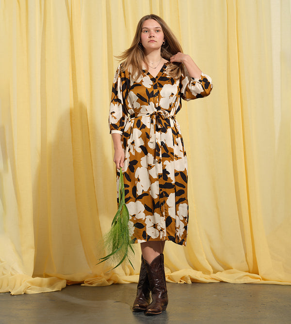 Liebling klänning Bonnie! Bonnie är en smula countryinspirerad i modellen. V-ringad, puffiga ärmar, fickor i sidorna och band att knyta i midjan. Rundat ok bak. Armbågslång ärm med smal manschett med en knapp. Svarta knappar mitt fram. Tyget är blankt vilket ger en lyxig känsla!&nbsp;

Färg: Vita blommor och svarta blad på guldbrun botten.&nbsp;

Material: 51% EcoVero, 49% viskos från Frankrike.