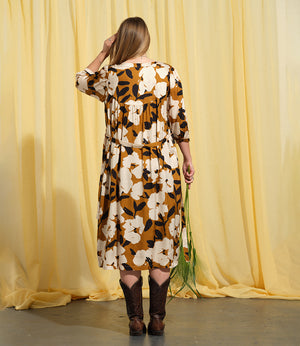 Liebling klänning Bonnie! Bonnie är en smula countryinspirerad i modellen. V-ringad, puffiga ärmar, fickor i sidorna och band att knyta i midjan. Rundat ok bak. Armbågslång ärm med smal manschett med en knapp. Svarta knappar mitt fram. Tyget är blankt vilket ger en lyxig känsla!&nbsp;

Färg: Vita blommor och svarta blad på guldbrun botten.&nbsp;

Material: 51% EcoVero, 49% viskos från Frankrike.