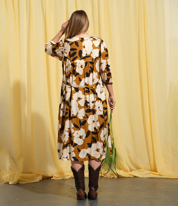 Liebling klänning Bonnie! Bonnie är en smula countryinspirerad i modellen. V-ringad, puffiga ärmar, fickor i sidorna och band att knyta i midjan. Rundat ok bak. Armbågslång ärm med smal manschett med en knapp. Svarta knappar mitt fram. Tyget är blankt vilket ger en lyxig känsla!&nbsp;

Färg: Vita blommor och svarta blad på guldbrun botten.&nbsp;

Material: 51% EcoVero, 49% viskos från Frankrike.