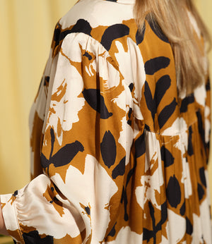 Liebling klänning Bonnie! Bonnie är en smula countryinspirerad i modellen. V-ringad, puffiga ärmar, fickor i sidorna och band att knyta i midjan. Rundat ok bak. Armbågslång ärm med smal manschett med en knapp. Svarta knappar mitt fram. Tyget är blankt vilket ger en lyxig känsla!&nbsp;

Färg: Vita blommor och svarta blad på guldbrun botten.&nbsp;

Material: 51% EcoVero, 49% viskos från Frankrike.