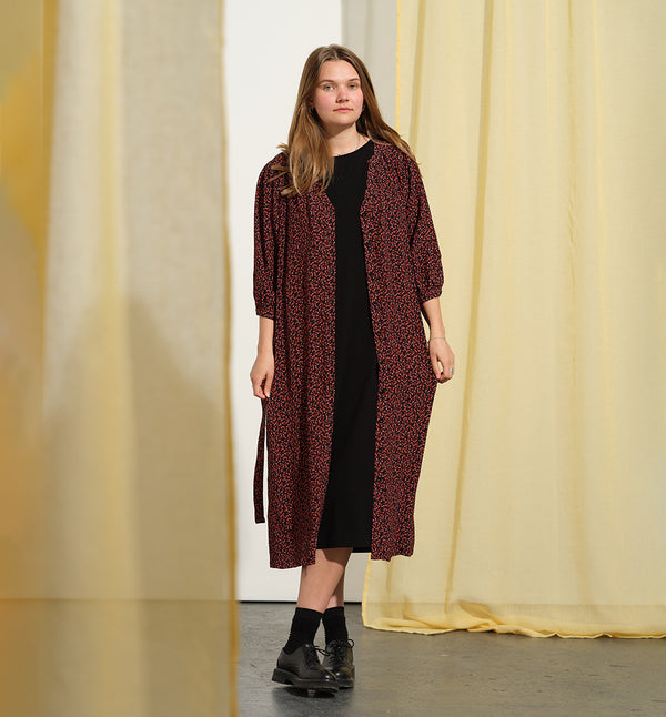 Liebling klänning Bonnie! Bonnie är en smula countryinspirerad i modellen. V-ringad, puffiga ärmar, fickor i sidorna och band att knyta i midjan. Rundat ok bak. Armbågslång ärm med smal manschett med en knapp. Svarta knappar mitt fram.

Färg: Små röda blommor på svart botten

Material: 51% EcoVero, 49% viskos från Frankrike.