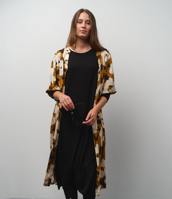 Vår klänning Bonnie! Bonnie är en smula countryinspirerad i modellen. V-ringad, puffiga ärmar, fickor i sidorna och band att knyta i midjan. Rundat ok bak. Armbågslång ärm med smal manschett med en knapp. Svarta knappar mitt fram. Tyget är blankt vilket ger en lyxig känsla!&nbsp;

Färg: Vita blommor och svarta blad på guldbrun botten.&nbsp;

Material: 51% EcoVero, 49% viskos från Frankrike.
Tillverkad i: Litauen
Designad i: Malmö