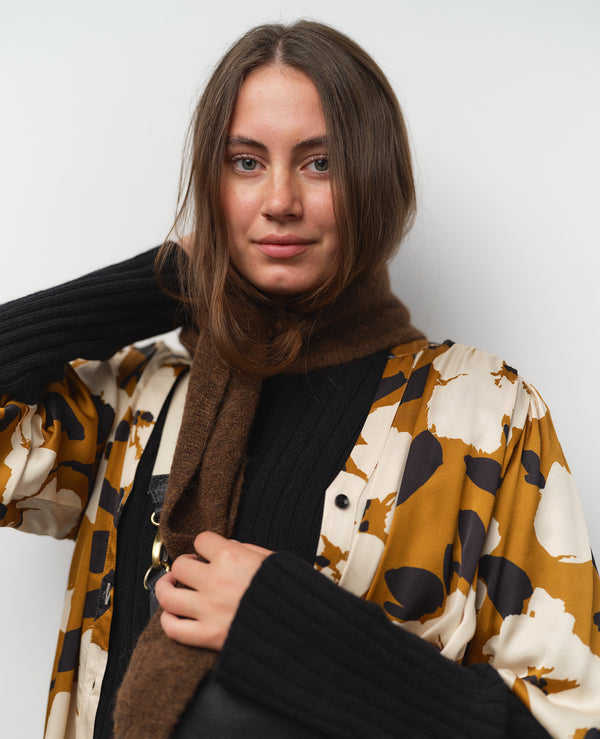 Vår klänning Bonnie! Bonnie är en smula countryinspirerad i modellen. V-ringad, puffiga ärmar, fickor i sidorna och band att knyta i midjan. Rundat ok bak. Armbågslång ärm med smal manschett med en knapp. Svarta knappar mitt fram. Tyget är blankt vilket ger en lyxig känsla!&nbsp;

Färg: Vita blommor och svarta blad på guldbrun botten.&nbsp;

Material: 51% EcoVero, 49% viskos från Frankrike.
Tillverkad i: Litauen
Designad i: Malmö