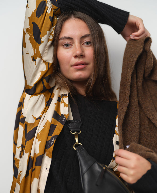 Vår klänning Bonnie! Bonnie är en smula countryinspirerad i modellen. V-ringad, puffiga ärmar, fickor i sidorna och band att knyta i midjan. Rundat ok bak. Armbågslång ärm med smal manschett med en knapp. Svarta knappar mitt fram. Tyget är blankt vilket ger en lyxig känsla!&nbsp;

Färg: Vita blommor och svarta blad på guldbrun botten.&nbsp;

Material: 51% EcoVero, 49% viskos från Frankrike.
Tillverkad i: Litauen
Designad i: Malmö