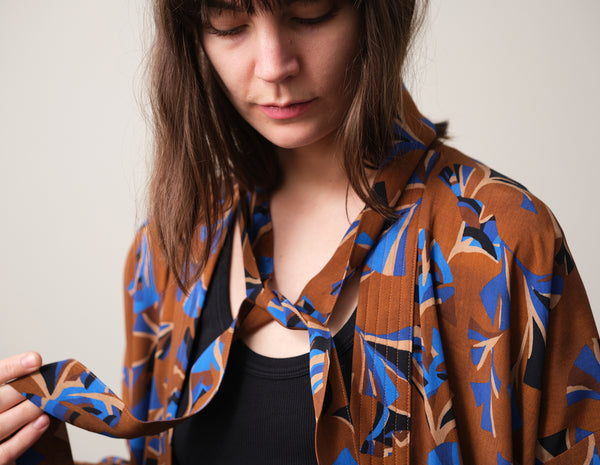 Lieblings kimono Gro i tyget Tosca. En lång lyxig kimono med fina kragdetaljer. Band att knyta i midjan. I kollektion Ridå har vi gjort Gro lite kortare än tidigare och i två storlekar. Tidigare onesize är nu S/M.&nbsp;

Färg: Mönster i kornblått, svart och beige på nougatbrun botten.

Material: 51% EcoVero, 49% viskos från Frankrike.