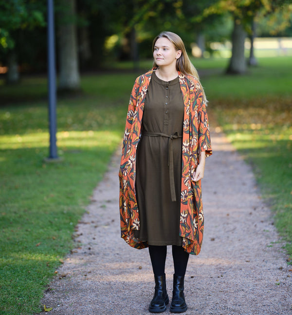 Lieblings kimono Gro i tyget Thalia. En lång lyxig kimono med fina kragdetaljer. Band att knyta i midjan.&nbsp;I kollektion Ridå har vi gjort Gro lite kortare än tidigare och i två storlekar. Tidigare onesize är nu S/M.&nbsp;

Färg: Blommor i grönt, gult, brunt och vitt på orange botten.

Material: 51% EcoVero, 49% viskos från Frankrike.