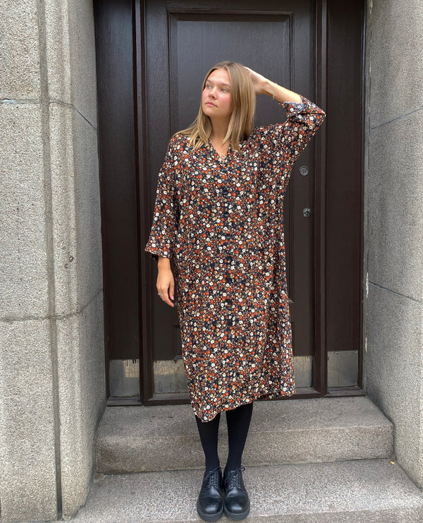 Klänningen Humla är en riktigt Lieblingfavorit. En ankellång kappklänning som kan bäras både öppen och stängd, som klänning eller kappa.&nbsp;Humla är en smula japaninspirerad i modellen och går att bära med eller utan det medföljande obi-bältet. Rak modell med krage, sprund bak och två fickor fram.&nbsp;

Färger: Små blommor i beige, vitt och orange på svart botten.

Material: 51% EcoVero, 49% viskos från Frankrike. 