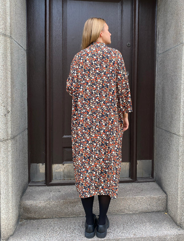 Klänningen Humla är en riktigt Lieblingfavorit. En ankellång kappklänning som kan bäras både öppen och stängd, som klänning eller kappa.&nbsp;Humla är en smula japaninspirerad i modellen och går att bära med eller utan det medföljande obi-bältet. Rak modell med krage, sprund bak och två fickor fram.&nbsp;

Färger: Små blommor i beige, vitt och orange på svart botten.

Material: 51% EcoVero, 49% viskos från Frankrike. 