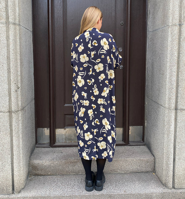 Klänningen Humla är en riktigt Lieblingfavorit. En ankellång kappklänning som kan bäras både öppen och stängd, som klänning eller kappa.&nbsp;Humla är en smula japaninspirerad i modellen och går att bära med eller utan det medföljande obi-bältet. Rak modell med krage, sprund bak och två fickor fram.&nbsp;

Färger: Gräddvita blommor med gula och olivgröna detaljer på mörkblå botten.

Material: 51% EcoVero, 49% viskos från Frankrike.