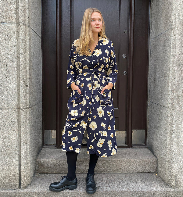 Klänningen Humla är en riktigt Lieblingfavorit. En ankellång kappklänning som kan bäras både öppen och stängd, som klänning eller kappa.&nbsp;Humla är en smula japaninspirerad i modellen och går att bära med eller utan det medföljande obi-bältet. Rak modell med krage, sprund bak och två fickor fram.&nbsp;

Färger: Gräddvita blommor med gula och olivgröna detaljer på mörkblå botten.

Material: 51% EcoVero, 49% viskos från Frankrike.