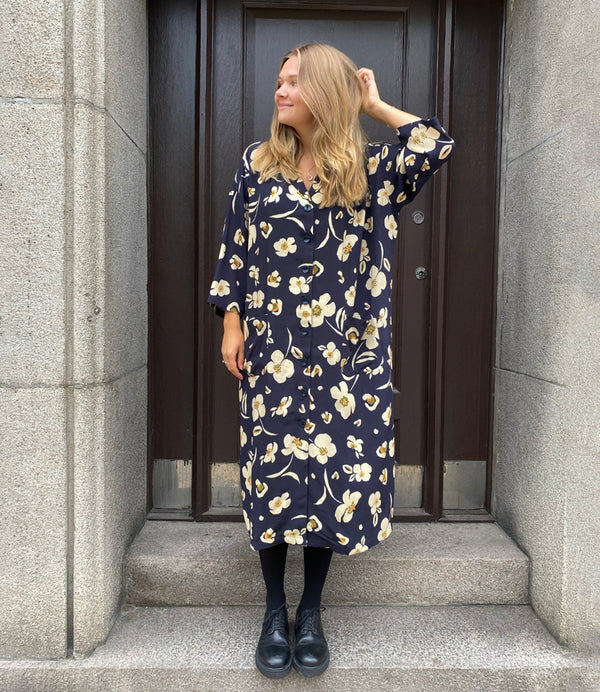 Klänningen Humla är en riktigt Lieblingfavorit. En ankellång kappklänning som kan bäras både öppen och stängd, som klänning eller kappa.&nbsp;Humla är en smula japaninspirerad i modellen och går att bära med eller utan det medföljande obi-bältet. Rak modell med krage, sprund bak och två fickor fram.&nbsp;

Färger: Gräddvita blommor med gula och olivgröna detaljer på mörkblå botten.

Material: 51% EcoVero, 49% viskos från Frankrike.