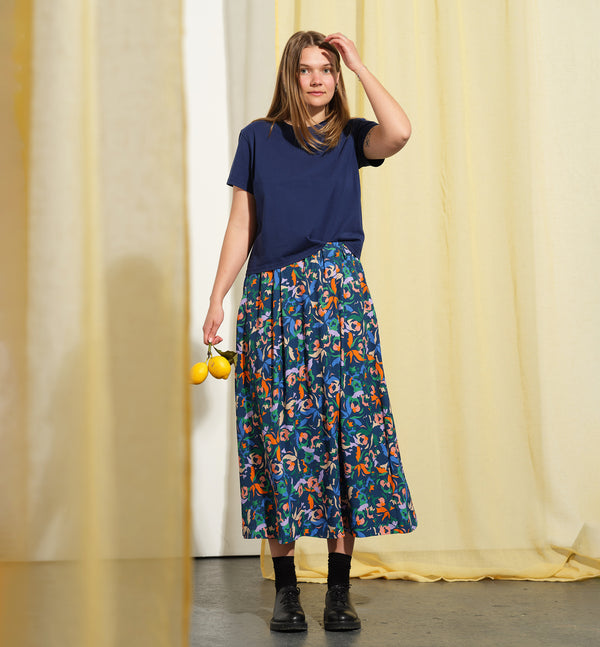 Kjolen Jojo! Avslappnad modell med veck fram, fickor i sidorna och resår med hällor i midjan. Sydd i en lyxig viskos med lite prickig struktur.&nbsp;

Färg: Blommor i orange, ljuslila, beige och klarblå på åskblå botten

Material: 51% EcoVero, 49% viskos från Frankrike.