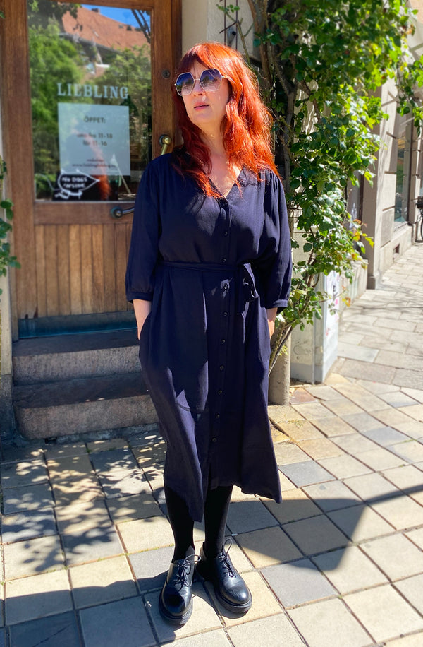  klänning Bonnie! Bonnie är en smula countryinspirerad i modellen. V-ringad, puffiga ärmar, fickor i sidorna och band att knyta i midjan. Rundat ok bak. Armbågslång ärm med smal manschett med en knapp. Svarta knappar mitt fram.&nbsp;

Färg: Riktigt mörkblå, nästan svart

Material: 100% viskos

Materialursprung:&nbsp;Detta tyg kommer från Italien.&nbsp;Deadstocktyg 