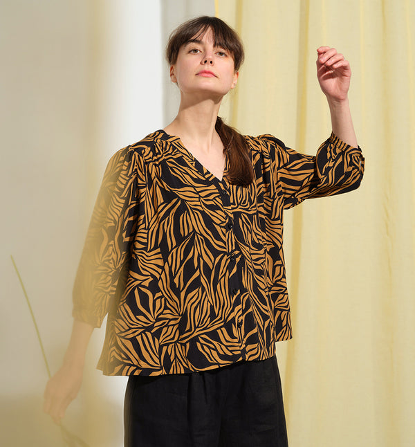  blus Lynn är en smula countryinspirerad i modellen. V-ringad, puffiga ärmar och rundat ok bak. Armbågslång ärm med smal manschett med en knapp. Svarta knappar mitt fram.

Färg: Ockragula palmblad på svart botten

Material: 51% EcoVero, 49% viskos från Frankrike