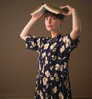  klänning Lyra. Murarkrage med avtagbart band. Knappslå fram med mörkblå knappar. Söm och rynk i midjan. Fickor i sidorna. Bandet knäpps på översta knappen. En fin detalj som ger Lyra fler stylingsmöjligheter. Sydd i en ekologisk viskos. Bandet ingår.

Färg: Gräddvita blommor med gula och olivgröna detaljer på mörkblå botten.

Material:&nbsp;51% EcoVero, 49% viskos från Frankrike. 