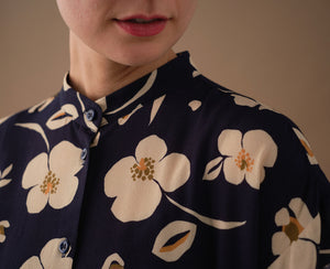  klänning Lyra. Murarkrage med avtagbart band. Knappslå fram med mörkblå knappar. Söm och rynk i midjan. Fickor i sidorna. Bandet knäpps på översta knappen. En fin detalj som ger Lyra fler stylingsmöjligheter. Sydd i en ekologisk viskos. Bandet ingår.

Färg: Gräddvita blommor med gula och olivgröna detaljer på mörkblå botten.

Material:&nbsp;51% EcoVero, 49% viskos från Frankrike. 