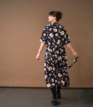  klänning Lyra. Murarkrage med avtagbart band. Knappslå fram med mörkblå knappar. Söm och rynk i midjan. Fickor i sidorna. Bandet knäpps på översta knappen. En fin detalj som ger Lyra fler stylingsmöjligheter. Sydd i en ekologisk viskos. Bandet ingår.

Färg: Gräddvita blommor med gula och olivgröna detaljer på mörkblå botten.

Material:&nbsp;51% EcoVero, 49% viskos från Frankrike. 