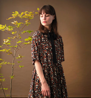 Lieblings klänning Lyra. Murarkrage med avtagbart band. Knappslå fram med svarta knappar. Söm och rynk i midjan. Fickor i sidorna. Bandet knäpps på översta knappen. En fin detalj som ger Lyra fler stylingsmöjligheter. Sydd i en ekologisk viskos. Bandet ingår.

Färg: Små blommor i beige, vitt och orange på svart botten.

Material:&nbsp;51% EcoVero, 49% viskos från Frankrike.