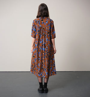 Vår klänning Sally i tyget Tosca.&nbsp;Sally är A-linjeformad med krage, knappslå, ok med små veck i ryggen och fickor i sidorna. Band att knyta i midjan.&nbsp;

Färg: Mönster i kornblått, svart och beige på nougatbrun botten.

Material: 51% EcoVero, 49% viskos från Frankrike.