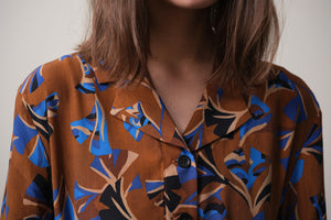 Vår klänning Sally i tyget Tosca.&nbsp;Sally är A-linjeformad med krage, knappslå, ok med små veck i ryggen och fickor i sidorna. Band att knyta i midjan.&nbsp;

Färg: Mönster i kornblått, svart och beige på nougatbrun botten.

Material: 51% EcoVero, 49% viskos från Frankrike.