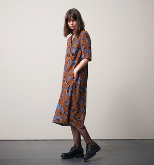 Vår klänning Sally i tyget Tosca.&nbsp;Sally är A-linjeformad med krage, knappslå, ok med små veck i ryggen och fickor i sidorna. Band att knyta i midjan.&nbsp;

Färg: Mönster i kornblått, svart och beige på nougatbrun botten.

Material: 51% EcoVero, 49% viskos från Frankrike.