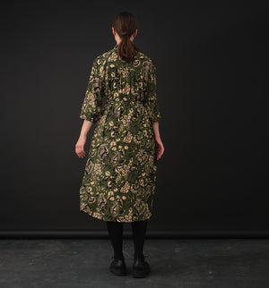 klänning Svala Lotus. En ankellång skjortklänning med lös passform, trekvartsärm och fickor i sidorna. Ok med rynk i ryggen. Ett 2,5 cm brett band i samma tyg medföljer och kan knytas i midjan. Svala är fin både öppen och stängd, med eller utan band. Svarta knappar mitt fram och vid ärmslut. Sydd i en fin viskos.

Svala&nbsp;är generös i storleken,&nbsp;välj gärna en storlek mindre än du brukar.
Se måttabell nedan.

Färg: Blommor i beige, svart och gulgrönt på grön botten.

Material:&nbsp;51% EcoVero, 49% v