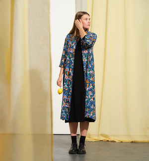 Vår klänning Svala Mimosa. En vadlång skjortklänning med lös passform, trekvartsärm och fickor i sidorna. Ok med rynk i ryggen. Ett 2,5 cm brett band i samma tyg medföljer och kan knytas i midjan. Svala är fin både öppen och stängd, med eller utan band. Svarta knappar mitt fram och vid ärmslut. Sydd i en fin viskos.

Färg: Blommor i orange, ljuslila, beige, grönt och klarblå på åskblå botten.

Material: 51%EcoVero, 49% viskos