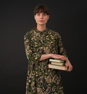 klänning Svala Lotus. En ankellång skjortklänning med lös passform, trekvartsärm och fickor i sidorna. Ok med rynk i ryggen. Ett 2,5 cm brett band i samma tyg medföljer och kan knytas i midjan. Svala är fin både öppen och stängd, med eller utan band. Svarta knappar mitt fram och vid ärmslut. Sydd i en fin viskos.

Svala&nbsp;är generös i storleken,&nbsp;välj gärna en storlek mindre än du brukar.
Se måttabell nedan.

Färg: Blommor i beige, svart och gulgrönt på grön botten.

Material:&nbsp;51% EcoVero, 49% v