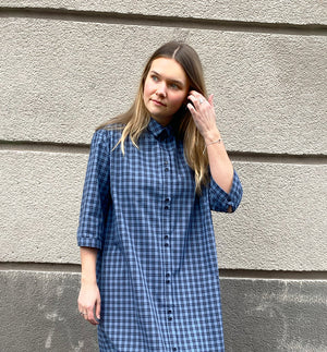 Vår klänning Svala. En ankellång skjortklänning med lös passform, trekvartsärm och fickor i sidorna. Ok med rynk i ryggen. Ett 2,5 cm brett band i samma tyg medföljer och kan knytas i midjan. Svala är fin både öppen och stängd, med eller utan band. Svarta knappar mitt fram och vid ärmslut. Sydd i ett deadstock tyg.&nbsp;

Färg: Svart och blårutig
Material: 100% bomull
Designad i Malmö, sydd i Litauen