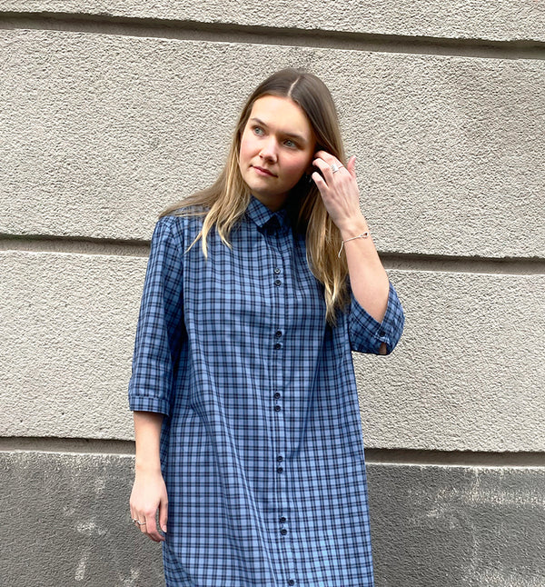 Vår klänning Svala. En ankellång skjortklänning med lös passform, trekvartsärm och fickor i sidorna. Ok med rynk i ryggen. Ett 2,5 cm brett band i samma tyg medföljer och kan knytas i midjan. Svala är fin både öppen och stängd, med eller utan band. Svarta knappar mitt fram och vid ärmslut. Sydd i ett deadstock tyg.&nbsp;

Färg: Svart och blårutig
Material: 100% bomull
Designad i Malmö, sydd i Litauen