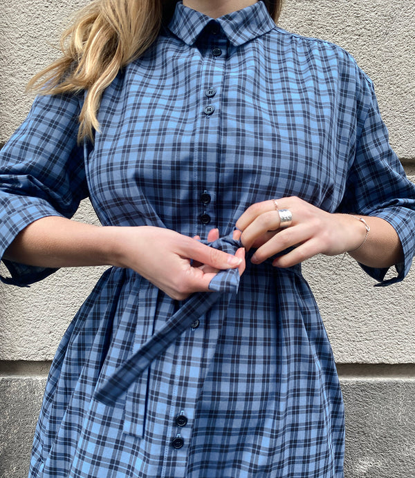 Vår klänning Svala. En ankellång skjortklänning med lös passform, trekvartsärm och fickor i sidorna. Ok med rynk i ryggen. Ett 2,5 cm brett band i samma tyg medföljer och kan knytas i midjan. Svala är fin både öppen och stängd, med eller utan band. Svarta knappar mitt fram och vid ärmslut. Sydd i ett deadstock tyg.&nbsp;

Färg: Svart och blårutig
Material: 100% bomull
Designad i Malmö, sydd i Litauen