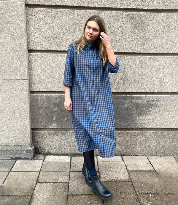 Vår klänning Svala. En ankellång skjortklänning med lös passform, trekvartsärm och fickor i sidorna. Ok med rynk i ryggen. Ett 2,5 cm brett band i samma tyg medföljer och kan knytas i midjan. Svala är fin både öppen och stängd, med eller utan band. Svarta knappar mitt fram och vid ärmslut. Sydd i ett deadstock tyg.&nbsp;

Färg: Svart och blårutig
Material: 100% bomull
Designad i Malmö, sydd i Litauen