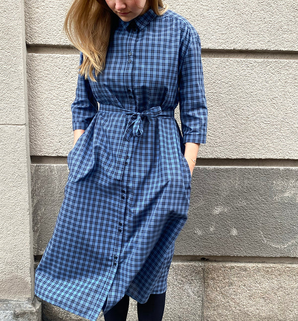 Vår klänning Svala. En ankellång skjortklänning med lös passform, trekvartsärm och fickor i sidorna. Ok med rynk i ryggen. Ett 2,5 cm brett band i samma tyg medföljer och kan knytas i midjan. Svala är fin både öppen och stängd, med eller utan band. Svarta knappar mitt fram och vid ärmslut. Sydd i ett deadstock tyg.&nbsp;

Färg: Svart och blårutig
Material: 100% bomull
Designad i Malmö, sydd i Litauen