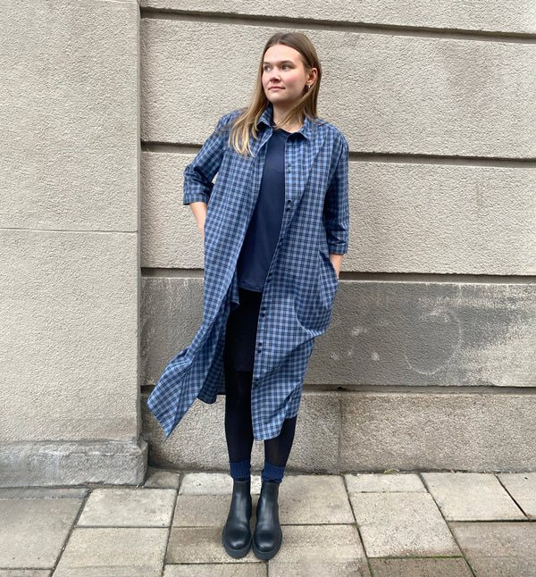 Vår klänning Svala. En ankellång skjortklänning med lös passform, trekvartsärm och fickor i sidorna. Ok med rynk i ryggen. Ett 2,5 cm brett band i samma tyg medföljer och kan knytas i midjan. Svala är fin både öppen och stängd, med eller utan band. Svarta knappar mitt fram och vid ärmslut. Sydd i ett deadstock tyg.&nbsp;

Färg: Svart och blårutig
Material: 100% bomull
Designad i Malmö, sydd i Litauen