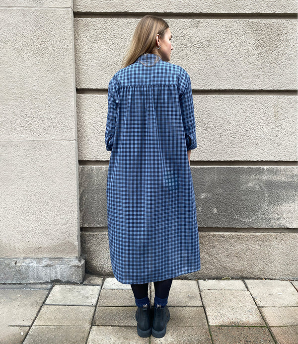 Vår klänning Svala. En ankellång skjortklänning med lös passform, trekvartsärm och fickor i sidorna. Ok med rynk i ryggen. Ett 2,5 cm brett band i samma tyg medföljer och kan knytas i midjan. Svala är fin både öppen och stängd, med eller utan band. Svarta knappar mitt fram och vid ärmslut. Sydd i ett deadstock tyg.&nbsp;

Färg: Svart och blårutig
Material: 100% bomull
Designad i Malmö, sydd i Litauen